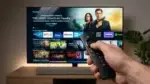 Primo piano di un telecomando Fire TV puntato verso uno schermo fluido e pulito, ambiente tech moderno.